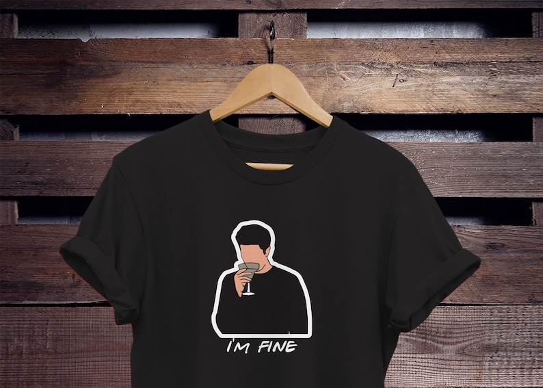 May include: Black t-shirt with a white outline of a cartoon character holding a glass of wine. The text "I'M FINE" is printed below the character.