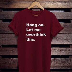 May include: A maroon t-shirt with white text that reads "Hang on. Let me overthink this."
