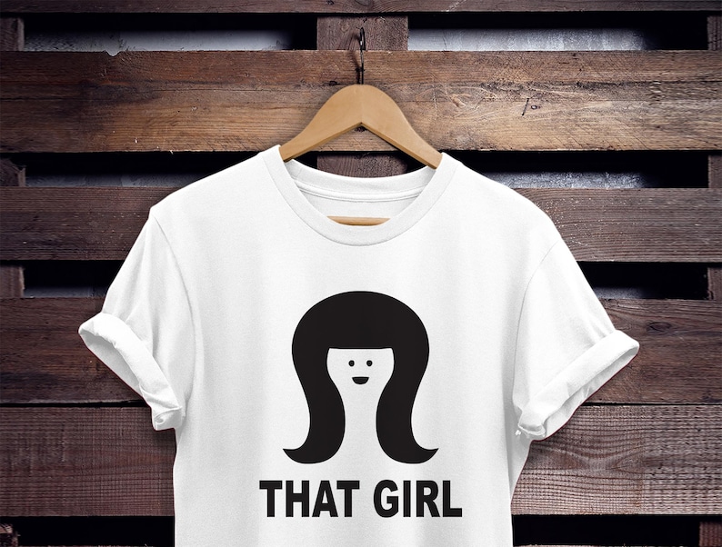 May include: White t-shirt with a black silhouette of a woman with a bob haircut and the text "THAT GIRL" printed on the front.