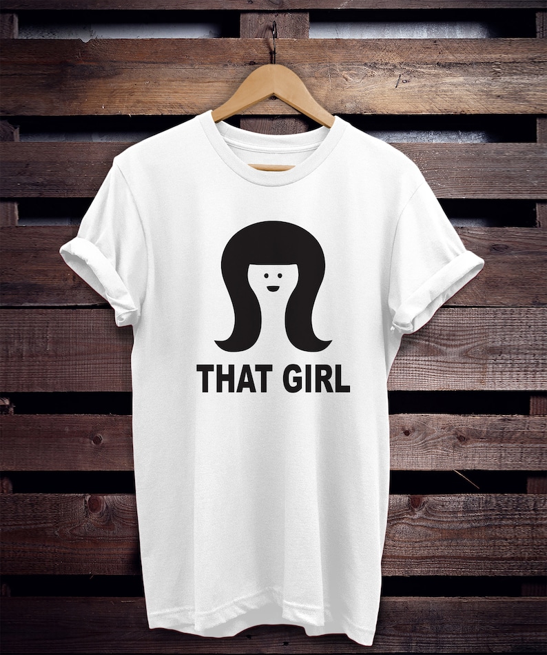 May include: White t-shirt with a black graphic of a woman with a bob haircut and the text "THAT GIRL".