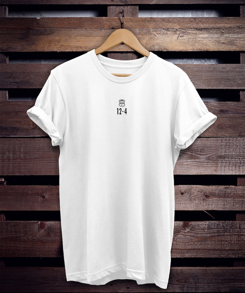 May include: White t-shirt with a black chef hat icon and the text "12-4" printed on the front.