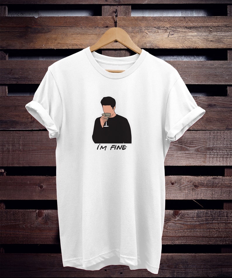 May include: White t-shirt with a black and white illustration of a person holding a glass of wine. The text "I'M FINE" is printed below the illustration.
