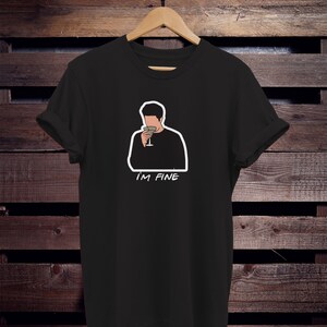May include: Black t-shirt with a white outline of a cartoon man holding a glass of wine. The text "I'M FINE" is printed below the image.