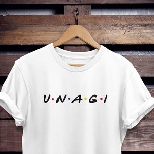 Könnte beinhalten: Weißes T-Shirt mit dem Text "U.N.A.G.I." in Schwarz mit farbigen Punkten.