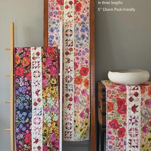 May include: Floral table runners in various lengths, displayed on wooden ladders. The runners feature vibrant patterns of red poppies, bluebells, and other flowers. The text indicates the table runners are 16.5 inches wide and charm pack-friendly.