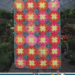 May include: A colorful quilt with a repeating pattern of starbursts in red, orange, pink, and yellow. The quilt is bordered with a green edge and features the text "BoBelynn" at the top. The bottom of the quilt has the text "Running Doe Quilts" and "For Villa Rosa Designs".