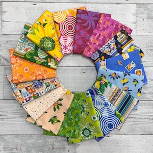 Puede incluir: Una colección de 12 cuadrados de tela coloridos con varios patrones, incluyendo limones, girasoles, edificios y paraguas. Los cuadrados de tela están dispuestos en un círculo sobre una superficie de madera blanca.