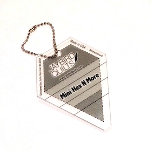 May include: A clear plastic hexagon-shaped ruler with a key ring. The ruler is labeled "Mini Hex N More" and "Jaybird Quilts". The ruler is designed for quilting and sewing.