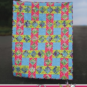 May include: A rectangular quilt featuring a repeating pattern of light blue, bright pink, and lime green fabric squares with multi-colored floral and abstract prints. The text "Loomed" appears at the top, and "Running Doe QUILTS For Villa Rosa Designs" with a white doe graphic is at the bottom.