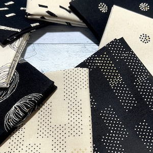 May include: A set of 10 fabric squares featuring geometric patterns in black, white, and gold. The fabric squares are arranged in a circle on a white wooden surface.