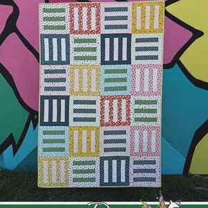 May include: A colorful quilt with a patchwork design. The quilt features squares in various colors, including blue, green, yellow, and pink, with dotted and striped patterns. The word "TURNKEY" is at the top, and the Running Doe Quilts logo is at the bottom.