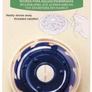May include: A Clover brand dome threaded needle case, Art No. 625, in cream and dark blue plastic. The circular case features a central hole and a notched outer rim for securing needles. It is presented on a beige cardboard backing with text.