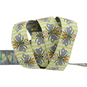 May include: A decorative ribbon with a repeating pattern of bees and hearts on a light green and white striped background. The ribbon is rolled up, showcasing the design. The bees have red and yellow details.