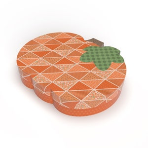 May include: Orange pumpkin-shaped box with a patchwork design featuring various patterns in orange, white, and brown. The top of the box has a green leaf with a brown stem.