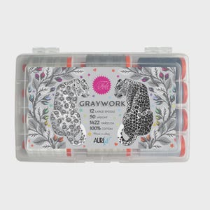 Puede incluir: Una caja de plástico transparente que contiene 12 carretes de hilo. La caja presenta una etiqueta decorativa con dos ilustraciones de leopardo y el texto "GRAYWORK". Los carretes son grises y azul marino con detalles en naranja. La etiqueta también indica "100% Algodón".