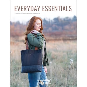 May include: A woman in a green jacket and blue jeans is holding a black and blue tote bag with brown leather straps. The bag has a small brown leather detail on the front. The text "EVERYDAY ESSENTIALS" is at the top of the image, and the text "noodlehead ANNA GRAHAM" is at the bottom of the image.