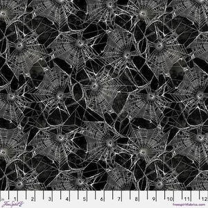 May include: A fabric with a repeating pattern of white spiderwebs on a dark gray and black background. The webs are detailed and intricate, creating a spooky, Halloween-themed design. The image includes a ruler along the bottom with inch measurements.