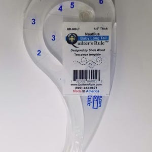 May include: A clear acrylic Nautilus Baby Long Tail Quilter's Rule template, 1/4 inch thick, featuring blue printed numbers 2 through 6 along its curved edges. A white product label is attached, displaying the text QR-NBLT, a barcode, and contact details.