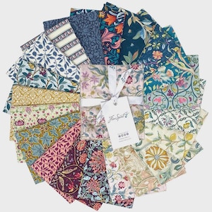 Pode incluir: Uma coleção de quadrados de tecido estampado em várias cores e desenhos florais. Os tecidos estão dispostos em um padrão circular, com um pacote central amarrado com uma fita branca e uma etiqueta que diz "Free Spirit".