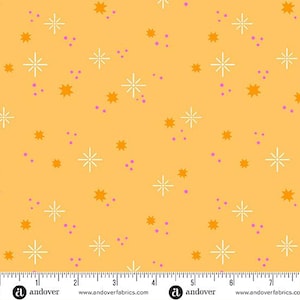 May include: A fabric with a repeating pattern of white starbursts, orange star shapes, and small purple dots on a yellow background. The fabric has a ruler along the bottom edge.