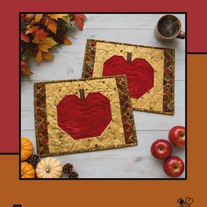 May include: Two rectangular quilted placemats featuring a central red apple motif on a gold background with a dark patterned border. The text Apples Mellow, Tamara Cook for Villa Rosa Designs is visible on the red and orange background.
