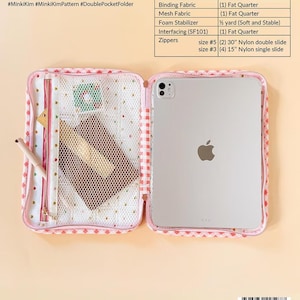 K&ouml;nnte beinhalten: Eine Stoffmappe mit zwei F&auml;chern und einem rosa-wei&szlig; karierten Rand, ausgestattet mit einer Netztasche und einem Tabletfach. Die Mappe ist ge&ouml;ffnet und zeigt ein helles Innenfutter mit einem kleinen Stoffrest und einem Stift.