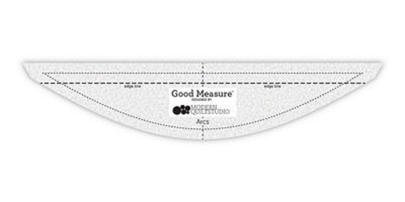 May include: A clear, arc-shaped quilting ruler with dotted and solid lines for measuring and cutting fabric. The ruler has the text "Good Measure" and "Designed by Modern Quilt Studio" printed on it. The tool is used for quilting.