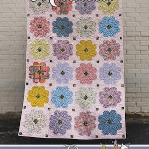 Pode incluir: Um edredom rosa com um padrão floral. O edredom apresenta grandes desenhos florais coloridos em tons de rosa, azul, amarelo e roxo. A palavra "Maureen" está escrita em itálico no topo. O edredom é da Running Doe Quilts.
