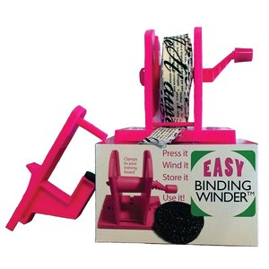 May include: A bright pink plastic binding winder tool with a hand crank, featuring a roll of cream-coloured fabric with black script text. The product packaging displays the text "EASY BINDING WINDER" and "Press it, Wind it, Store it, Use it!"