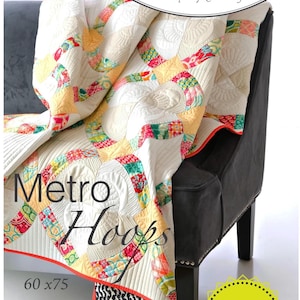 Op de afbeelding: Een quiltpatroon genaamd "Metro Hoops" van Sew Kind of Wonderful. De quilt heeft een witte achtergrond met kleurrijke patchwork-vierkanten en een rode rand. De quilt is 60 inch bij 75 inch. Het patroon is beschikbaar als digitale download.