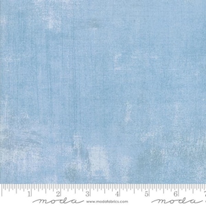 May include: A light blue fabric with a subtle textured pattern. The fabric has a slightly distressed look, with faded areas and a hint of white throughout. The fabric is perfect for quilting, crafts, and home decor projects.
