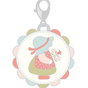 Könnte beinhalten: Ein runder Charm mit einem gewellten Rand in Pastellfarben. Der Charm zeigt ein Mädchen mit Häubchen, das Blumen hält. Das Kleid des Mädchens ist rosa und grün, und der Charm hat einen silbernen Verschluss.