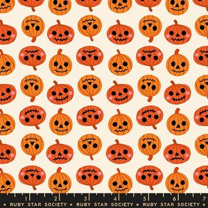 Puede incluir: Una tela de color crema con un patrón repetitivo de calabazas de Halloween naranjas con rasgos faciales negros y mejillas rosadas. Una regla negra con marcas blancas y el texto Ruby Star Society es visible en el borde inferior.