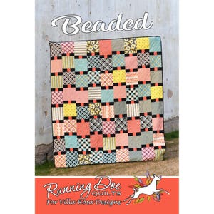 Pode incluir: Um edredom colorido com um design de patchwork com quadrados em vários padrões e cores, incluindo rosa, amarelo, azul e preto. A palavra "Beaded" está escrita em itálico no topo. O edredom é da Running Doe Quilts.