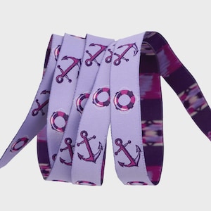 May include: A coiled ribbon featuring a nautical design. The light purple ribbon is adorned with repeating patterns of purple anchors and life preservers. The reverse side of the ribbon has a dark purple and pink abstract pattern.
