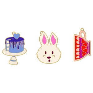 May include: Three enamel pins: a blue cake with a heart, a white rabbit head with pink ears, and a red and pink teacup. Each pin has a gold outline and is set against a white background.