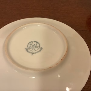 Może przedstawiać: Biały talerz porcelanowy z falistym brzegiem. Sp&oacute;d zdobi niebiesko-białe logo z napisem "RW Bavaria 77 Handgemalt."