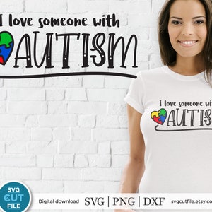Puede incluir: Camiseta blanca con el texto "I love someone with AUTISM" en escritura negra. Un diseño de rompecabezas en forma de corazón colorido está encima de la palabra "AUTISM". El mismo texto y diseño también están en la pared.