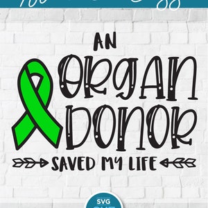 May include: Green ribbon with the text "An Organ Donor Saved My Life" in black lettering. The text is surrounded by arrows pointing to the left and right. The image includes the text "SVG CUT FILE" in a blue circle.