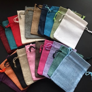 May include: A collection of small, drawstring bags made of burlap in various colors, including red, blue, green, purple, and brown. The bags are arranged in a fan shape on a black surface.