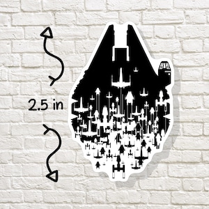 May include: A black and white sticker featuring a silhouette of the Millennium Falcon with various starfighters. The sticker is approximately 2.5 inches in height. The design is set against a white background.