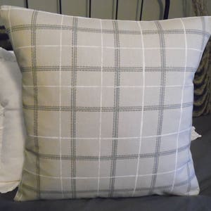 May include: A beige pillow with a white and gray plaid pattern. The pillow is made of a soft, woven fabric and has a subtle sheen.