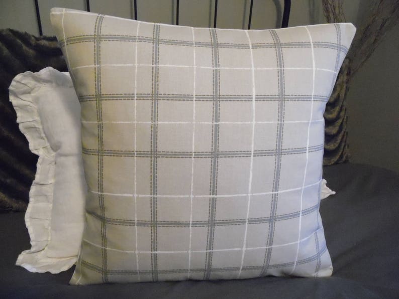 May include: A beige pillow with a white and gray plaid pattern. The pillow is made of a soft, woven fabric and has a subtle sheen.