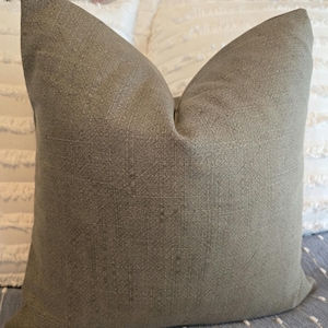 May include: A soft, green throw pillow with a textured fabric. The pillow is sitting on a white and gray patterned surface.