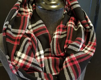 Könnte beinhalten: Ein schwarzer, roter und weiß karierter Loop-Schal auf einer Schaufensterpuppe. Der Schal ist aus einem weichen Stoff gefertigt und weist ein klassisches Karomuster auf. Der Schal ist um den Hals der Schaufensterpuppe gewickelt und zeigt sein Design.