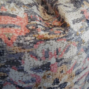 May include: Close-up of a fabric with a patterned design featuring shades of pink, gray, and beige. The fabric has a textured surface and a slightly wrinkled appearance.