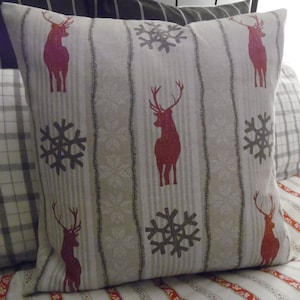 May include: Square decorative pillow with a cream background and vertical stripes. The pillow features red deer silhouettes and gray snowflakes. The pillow is part of a set of pillows with different patterns.