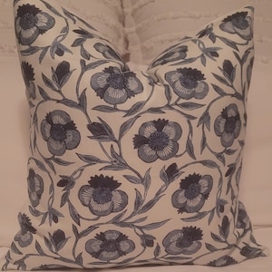 May include: A white pillow with a blue floral pattern. The flowers are stylized and have a dark blue center. The pillow is made of a soft, comfortable fabric.