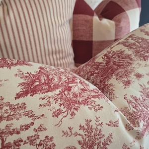 May include: Three decorative throw pillows with a red and white striped pattern, a red and white gingham pattern, and a white background with a red toile pattern.