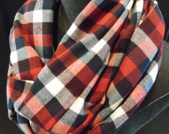 Könnte beinhalten: Rote, schwarze und weiße karierte Infinity-Schal. Der Schal ist aus einem weichen, bequemen Stoff gefertigt und perfekt, um sich im Winter warm zu halten.